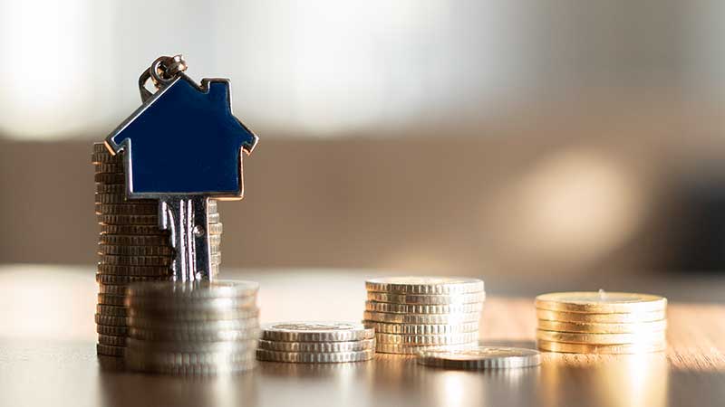 Montinhos de moedas com chave de casa pendurada no maior